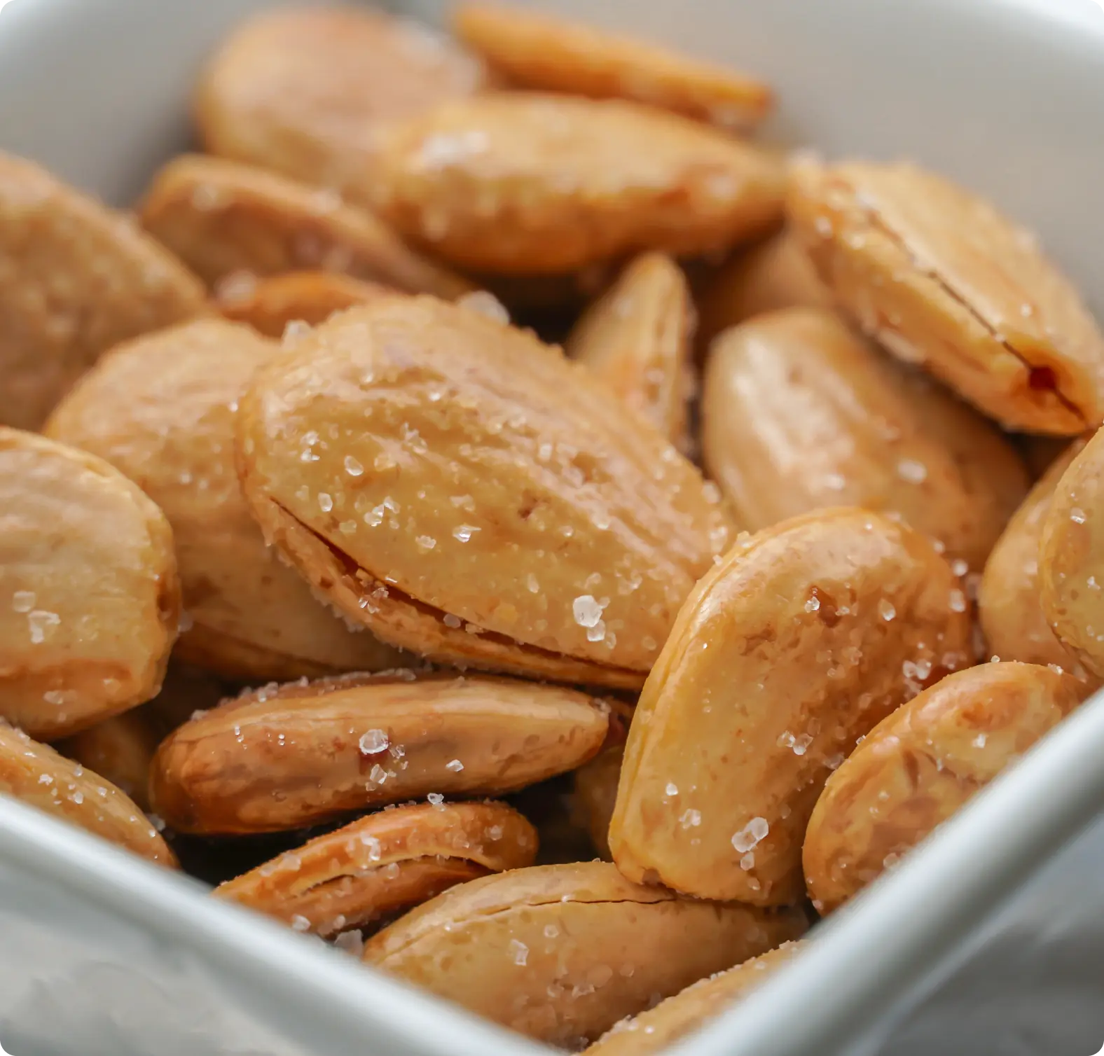 Close-up of salted almonds in a white bowl.