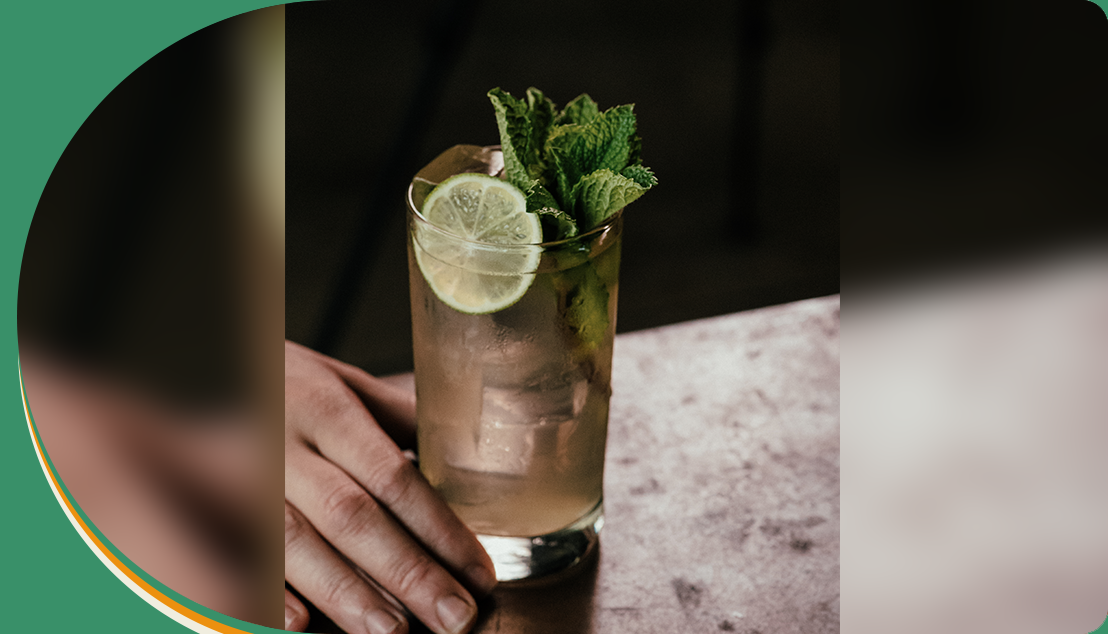 A person holding a glass of drink with lime and mint.