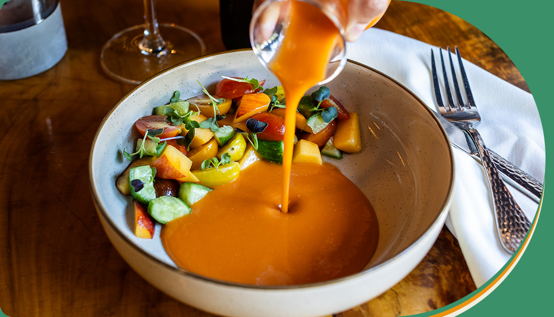 A person pouring orange juice into a bowl of salad.