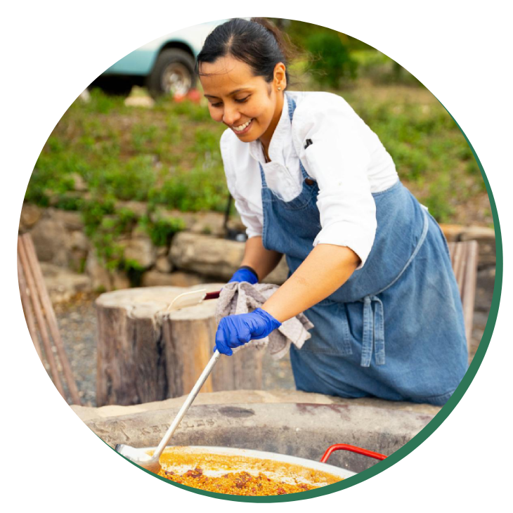 A woman in an apron is cooking food on the grill.